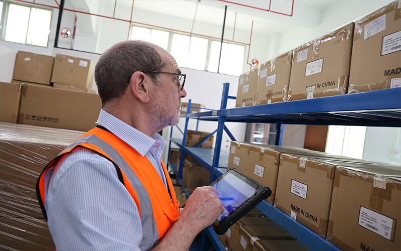Heavy duty industrial tablet computer used for inventory tracking and barcode scanning in a modern logistics warehouse.