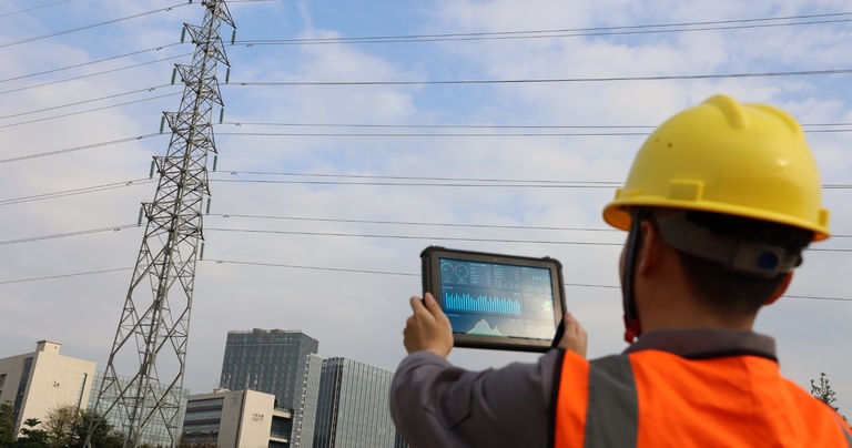 Field technician using a rugged tablet for power line inspection and utility asset management.